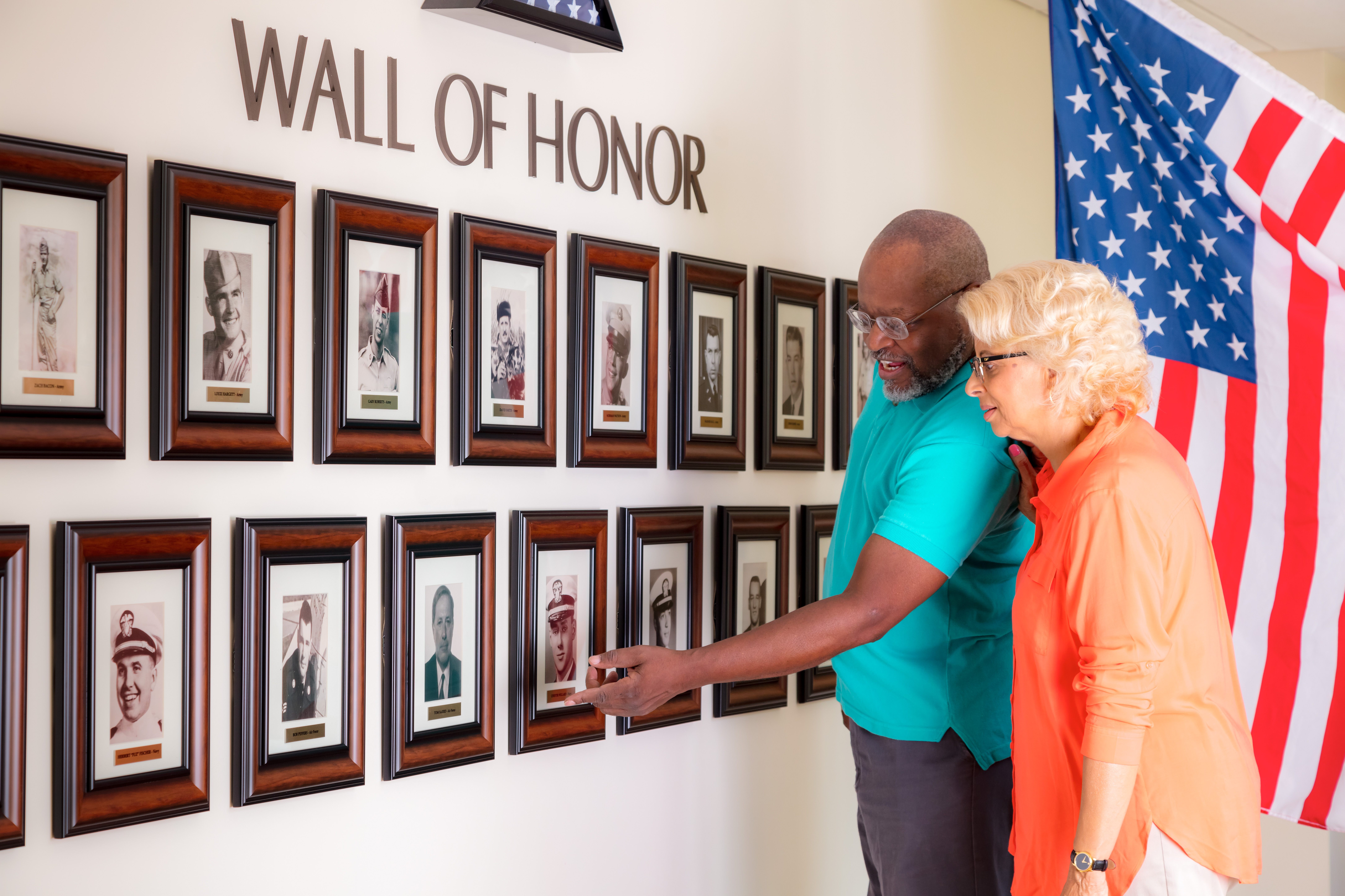 Cardinal residents talking and pointing to pictures on the community's Wall of Honor featuring photos of veterans who live at the community.