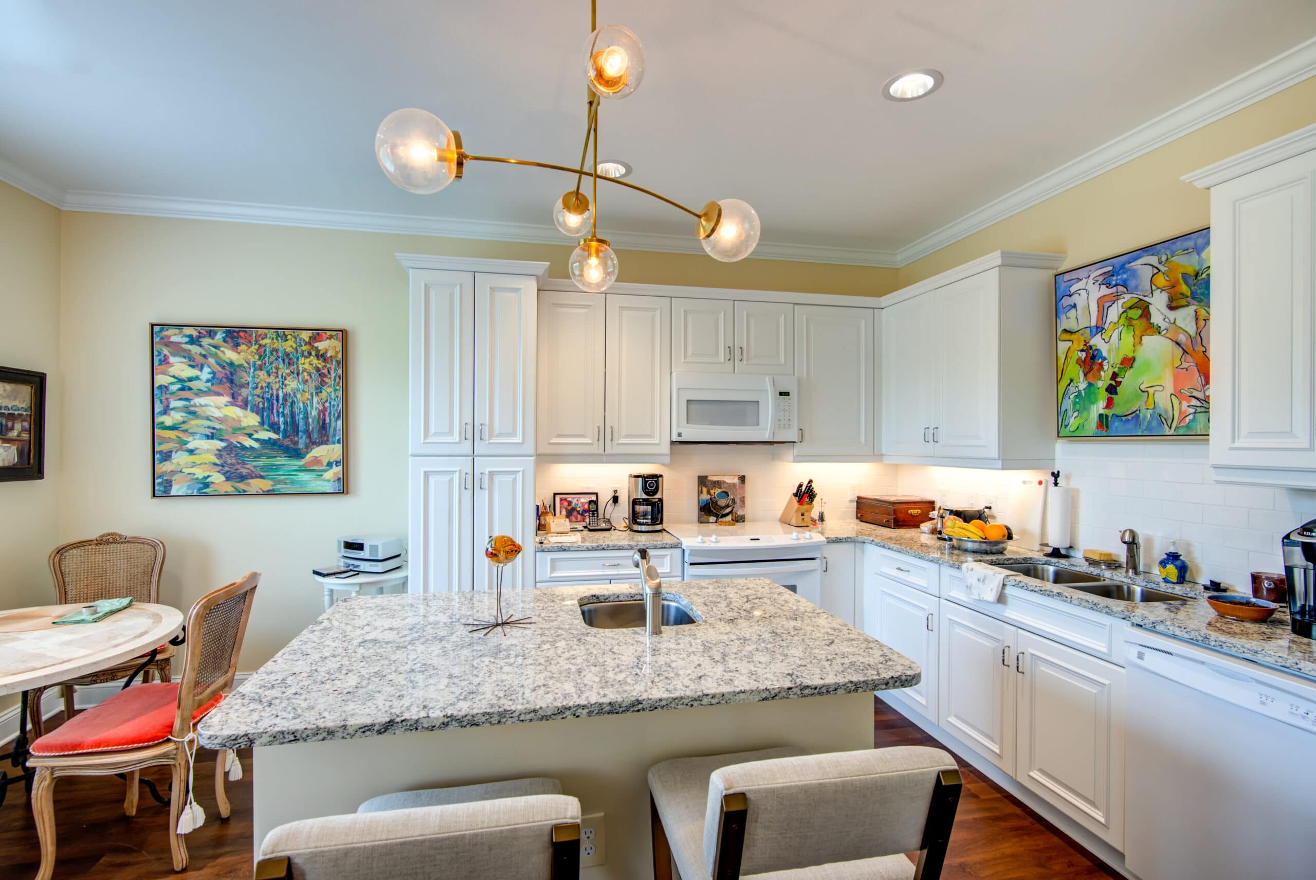 Interior of an independent living kitchen featuring hardwood floors, white cabinets and marble countertops.