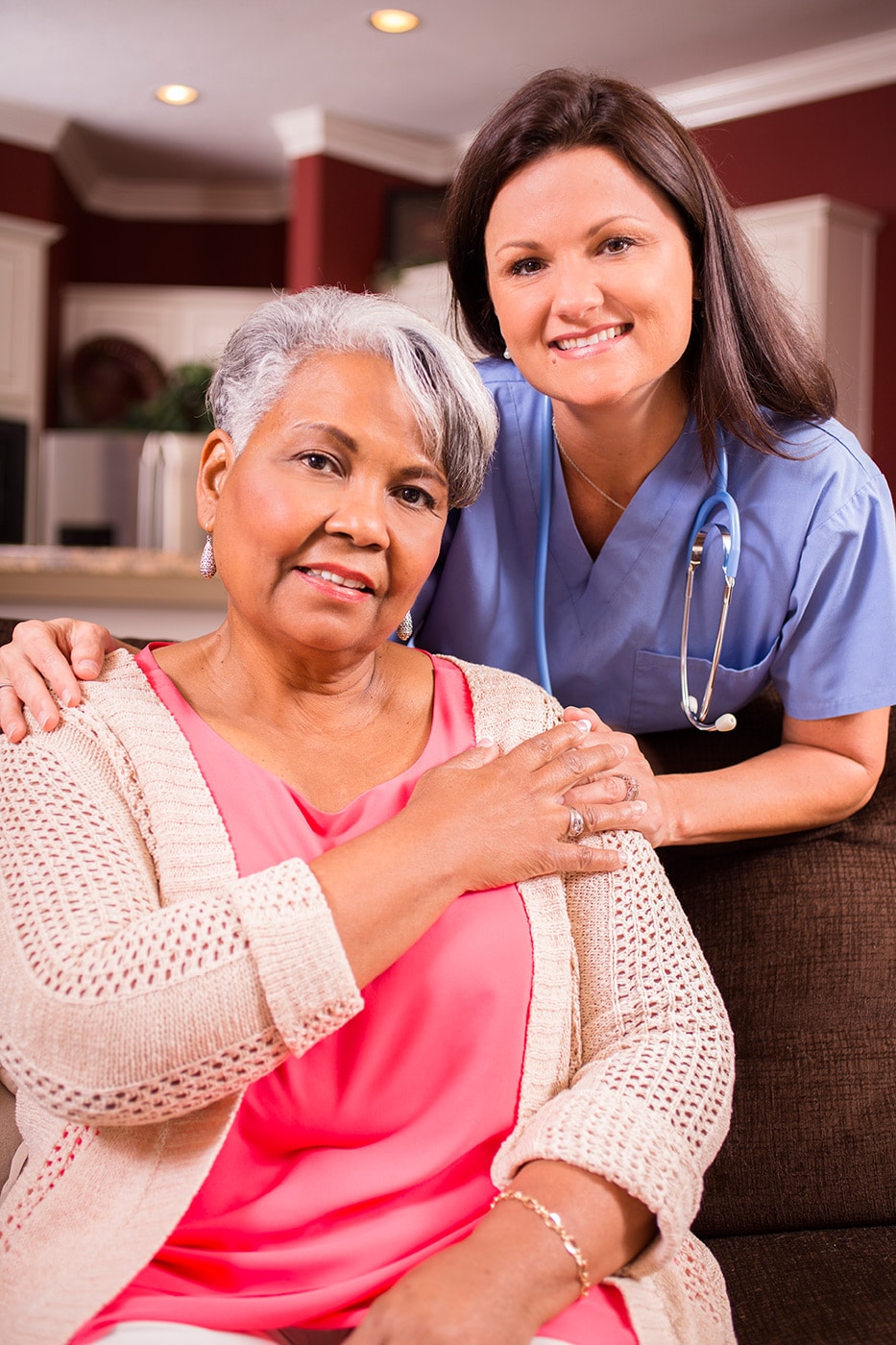 Older woman smiles while placing her hand over the hand of a younger nurse.