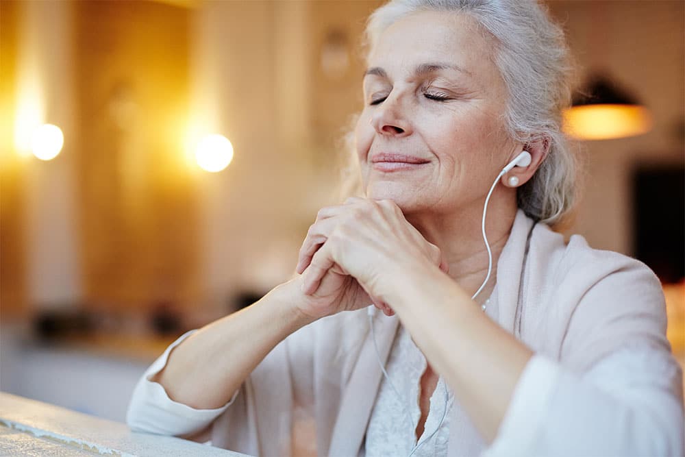 Woman smiling contently with hand folded under her chin listening to music with headphones.