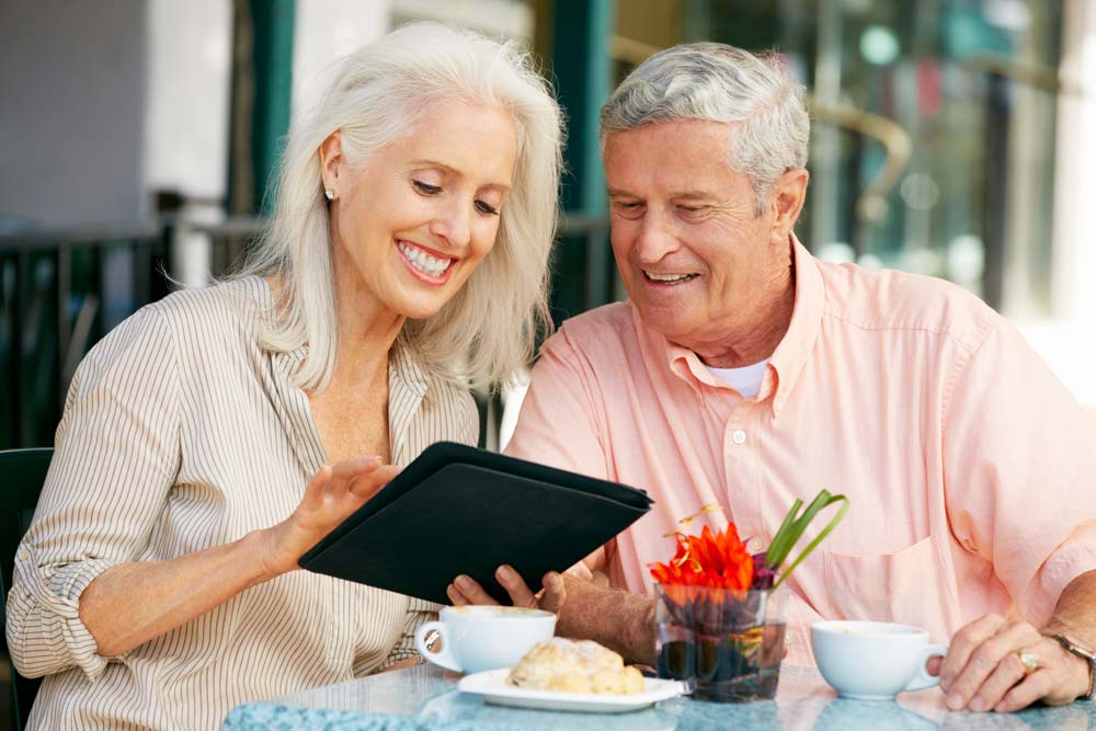 Couple smiling and looking at something on a tablet computer while having some coffee and breakfast.