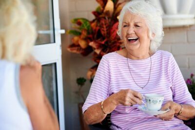 Happy woman enjoying a cup of tea and laughing with a friend